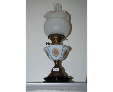 An oil lamp standing on a circular base with metal column leading to white glass reservoir with floral decoration and white s
