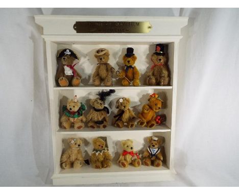 A wall mounted display case with plaque marked The Teddy Bear  Museum Showcase containing twelve dressed miniature bears