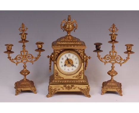 A circa 1900 gilt brass three piece clock garniture, the clock surmounted with a pedestal urn, having a white enamel dial, Ar