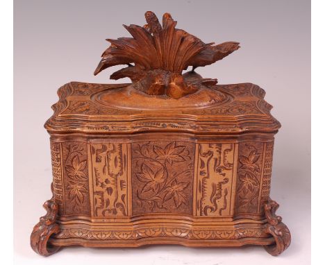 A late 19th century Black Forest carved tea caddy, of serpentine outline,the hinged cover surmounted with game birds, the who