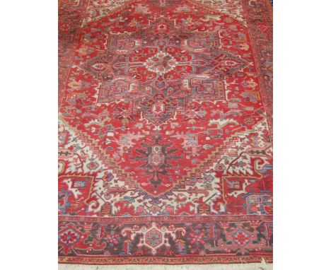 A Kadjar woollen carpet, the red ground with centre geometric motif issuing scroll flowers and foliage within trailing tramli