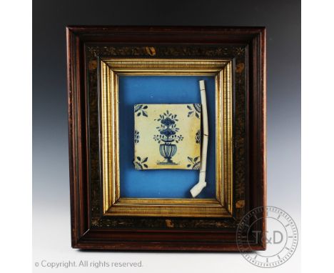 A 17th century Delft tile decorated with blue floral sprays in a vase, and pipe, 13cm x 13cm (restored) and a clay pipe, 23cm