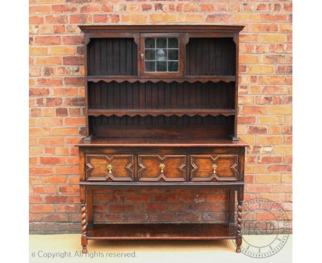 A 1920's oak dresser, the raised back with a central lead glazed door, above three fielded drawers and a pot shelf, on barley