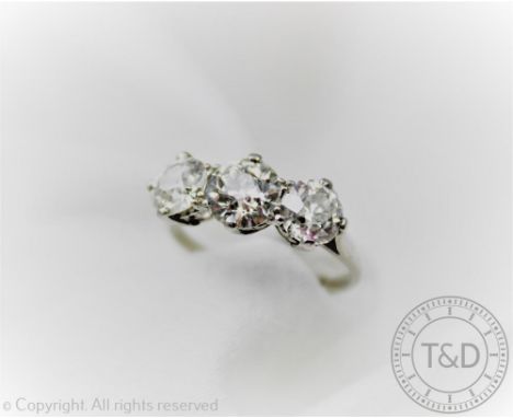 A three stone diamond ring, the three graduated old brilliant cut diamonds each set within white metal claw setting to the ta