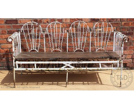 A wrought iron garden bench, possibly French, the four section arched back with brass finials, with scroll end arms and box s