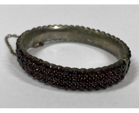 VINTAGE THREE ROW GARNET BANGLE IN WHITE METAL - with gilt metal safety chain, 6.5cms across