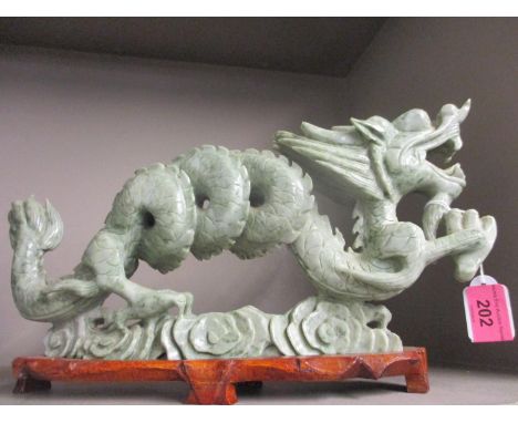 A Chinese carved model of a dragon in light green soapstone mounted on a wooden stand 