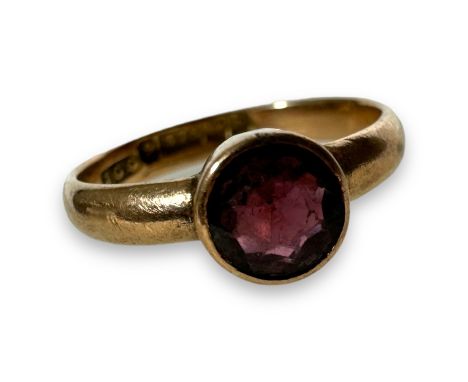 A 9ct gold garnet set solitaire ring. Featuring a dark red round mixed cut bezel set stone, in 9ct gold marked for Birmingham