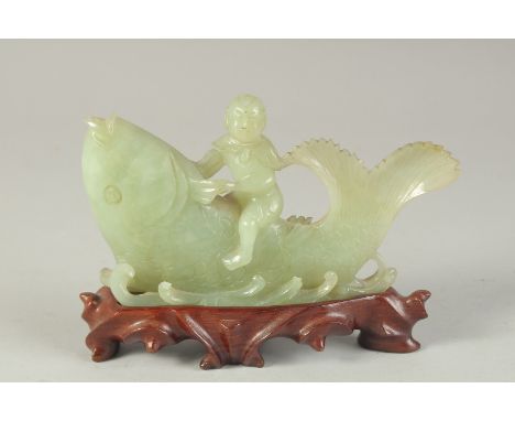A CHINESE CARVED JADE FIGURAL GROUP of a boy riding a giant fish, on a fitted carved hardwood stand, 16cm wide.