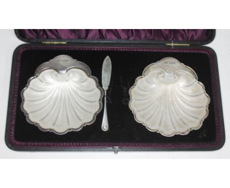 A cased pair of silver half clam butter dishes with glass liners and one knife, Levesley Brothers, Sheffield 1923.  