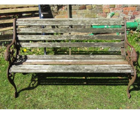 A two to three seat garden bench with weathered timber lathes raised on a pair of decorative pierced cast iron ends with lion