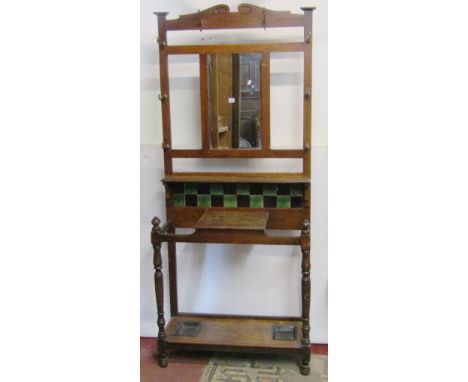 An Edwardian oak hall stand of full height enclosing a bevelled edge mirror plate with ceramic tiled back