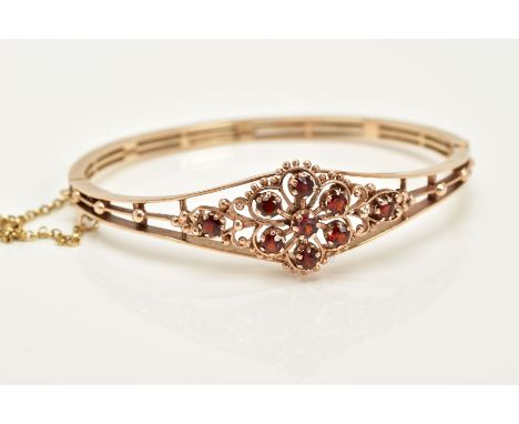 A 9CT GOLD GARNET SET OPENWORK BANGLE, the openwork hinged bangle of floral design, set with circular cut garnets, with bead 