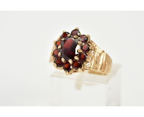 A 9CT GOLD GARNET CLUSTER RING, the raised cluster designed with a central oval cut garnet, within a circular cut garnet surr
