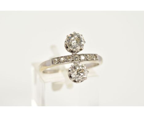 AN EARLY 20TH CENTURY TWO STONE DIAMOND RING, the white metal ring designed with a quarter row of single cut diamonds, flanke