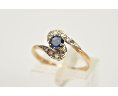 A 9CT GOLD SAPPHIRE AND DIAMOND RING, a cross over design, set with a central circular cut sapphire, flanked with single cut 