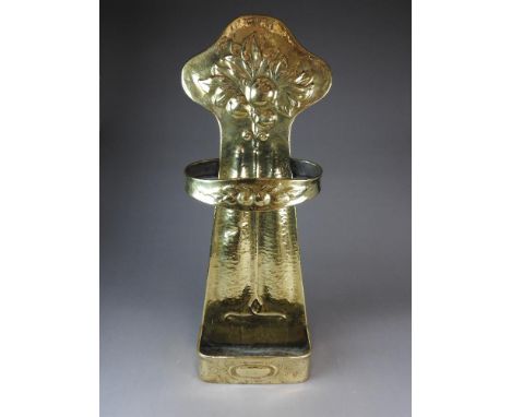 An Arts and Crafts brass stick stand, late 19th century, embossed with a floral design on a shaped rear bracket and with rect