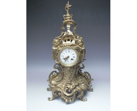 A BRASS ROCCOCO STYLE MANTEL CLOCK, scrolling form with cherubic and mask decoration, circular dial with blue Roman numerals 