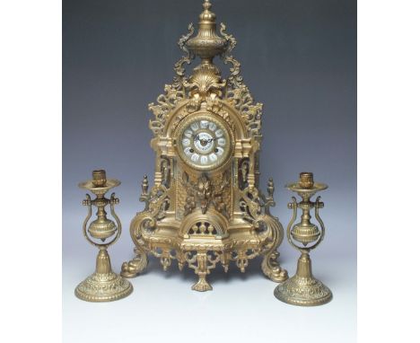 AN ORNATE BRASS MANTEL CLOCK WITH MATCHED CANDLESTICKS, the case with pierced decoration throughout and urn surmount, the dia