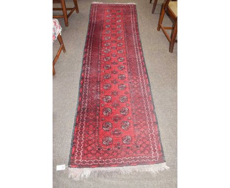 An Afghan Turkmen runner, the scarlet field with two columns of guls. enclosed by geometric borders, 279cm by 86cm; together 