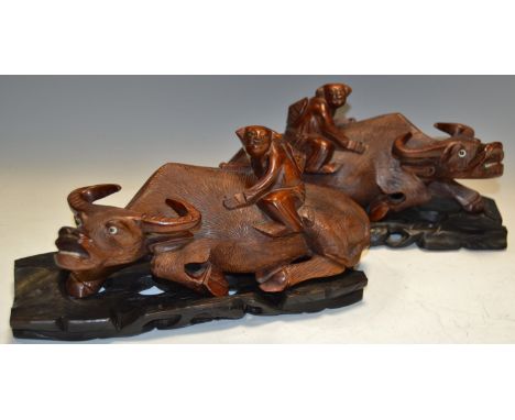 A pair of Chinese hardwood carvings, of boys astride water buffaloes, the beasts with inset glass eyes, ebonised hardwood pie