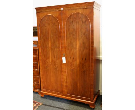 A contemporary yew double wardrobe, ogee cornice above arched fielded doors, bracket feet, castors (Key with Porter)