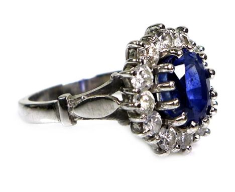 An 18ct white gold dress ring, set with an oval cut sapphire, approximately 8 by 6 by 5mm, surrounded by twelve circular cut 