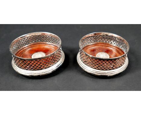 A pair of ERII silver wine bottle coasters, with pierced lattice sides and turned mahogany bases inset with a circular silver