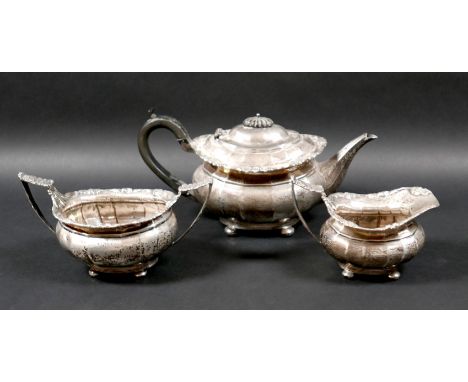 An George V silver three piece tea service, with faceted bodies and fruiting vine cast rims, comprising teapot with ebonised 