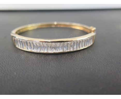 A 9ct gold cubic zirconia hinged bangle - The baguette-cut cubic zirconias within a channel setting - Hallmarked London - Inn