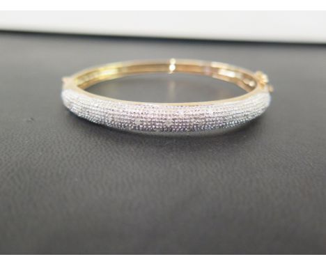 A 9ct bi-colour gold diamond hinged bangle -  The brilliant-cut diamond highlights to the textured surmount - Diamond weight 