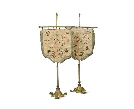 A pair of tapestry and 'gilt' metal table screens, late 19th century, on triform foliate bases, the shield-shaped screens wor