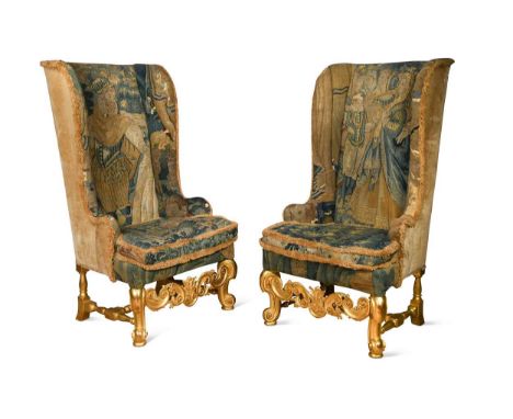 A pair of Carolean-style carved giltwood wingback armchairs, 19th/20th century, raised on scrolled feet united by a carved ap