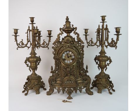 A LARGE GILT METAL CLOCK GARNITUREThe clock with Roman numerals and central mask decoration, the twin gong movement marked FH