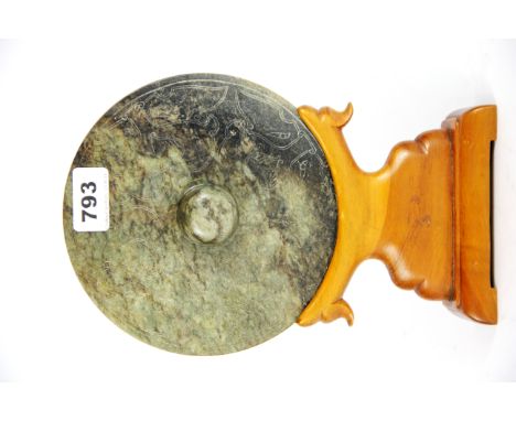 A Sino-Tibetan carved jade mirror style object on a carved wooden stand, Dia. 18cm. Prov. Bynon Estate.