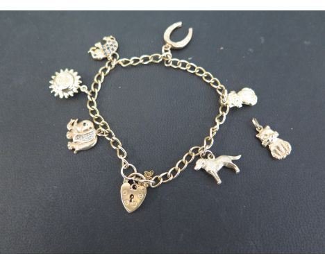 A 9ct gold curb-link chain suspending six assorted charms - Together with a further loose charm - Hallmarked Birmingham - Len