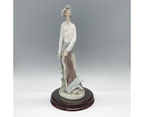 Glossy figurine of Don Quixote standing proudly, clutching a sword, accompanied by armor and books. Lladro backstamp. This it