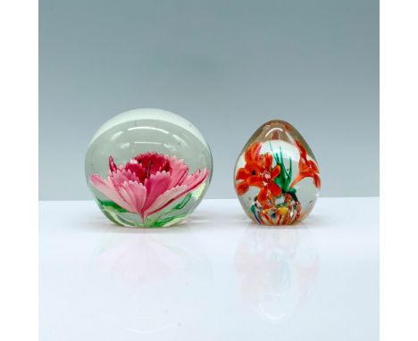 A set of two clear glass paperweights with floral artwork, one containing a large pink flower with black stigmas, the other i