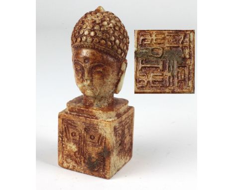 A Qing period Jade Seal, in the form of a Buddha head with double face, on square block base with taotie pattern, 6" (15cms).