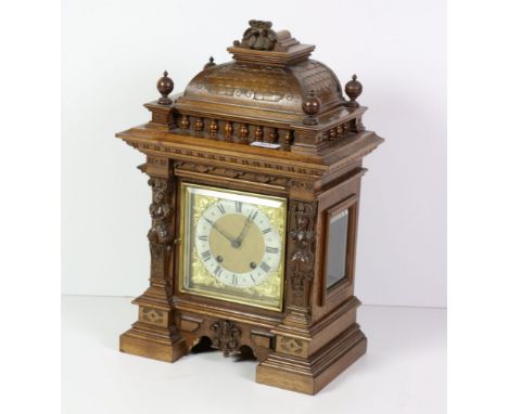 An Edwardian carved walnut Mantle Clock, the square brass dial with silver chapter ring, flanked by two carved female figures