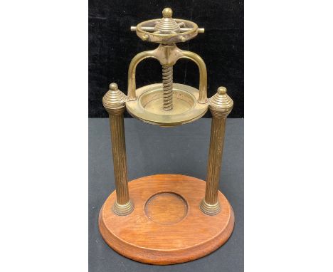 An early 20th century brass citrus fruit juicer, ship's wheel screw action compressor, the pierced basin supported by a pair 