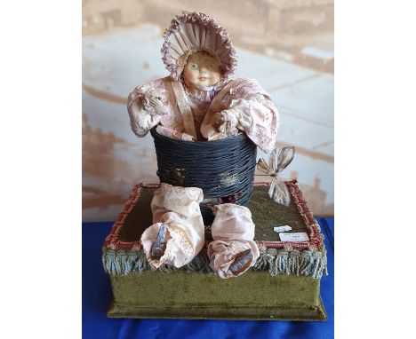 An early 20th Century antique style musical automaton, in the form of a macabre baby doll in basket; clothed in Victorian sty
