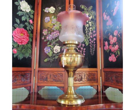 An early 20th century brass oil lamp, having cranberry and frosted glass shade, 59cm.