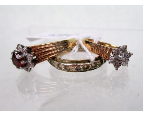 A diamond cluster ring, illusion set in textured bark finish mount, together with a garnet cluster ring and one other.