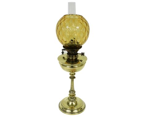 A late 19th/early 20thC oil lamp, with a later amber coloured glass shade, a brass central reservoir and an Art Nouveau patte