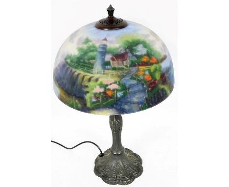 A Thomas Kinkade table lamp, the reverse decorated shade decorated with a cottage, lighthouse and sea scape, on a cast metal 