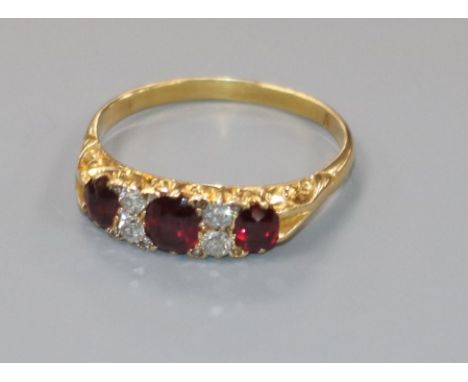 An early-mid 20th century yellow metal three stone ruby and four stone diamond ring, size S.