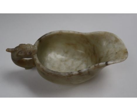 A Chinese marbled white jade jug, of archaic form, with a shaped bowl on an oval foot with a carved handle, 11.5cm long CONDI