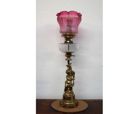 An oil lamp with a graded red to clear glass shade with a clear glass reservoir, the gilt metal base in the form of a cherub 