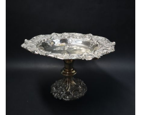 A late Victorian silver pedestal dish, the border embossed with scrolls, flowerheads and leaves, with a ring turned column an